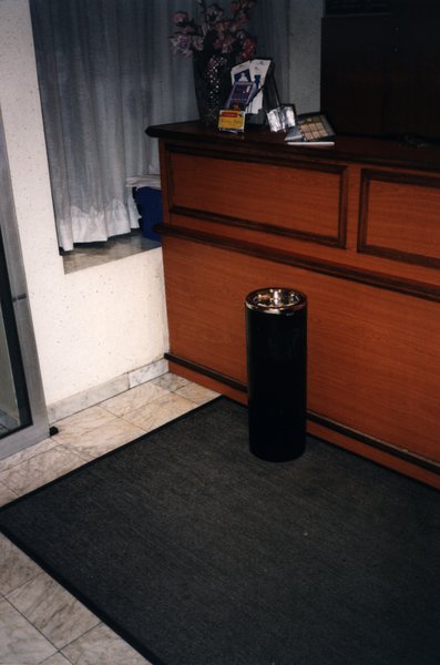 Cendrier cylindrique noir posé sur un tapis devant un comptoir en bois.ᴬᴵ