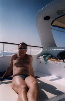Homme en maillot de bain assis sur le pont d’un bateau.