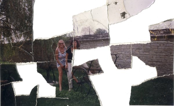 Deux femmes brunes et blondes assises à califourchon sur une vieille charrue. Image déchirée en partie reconstituée.