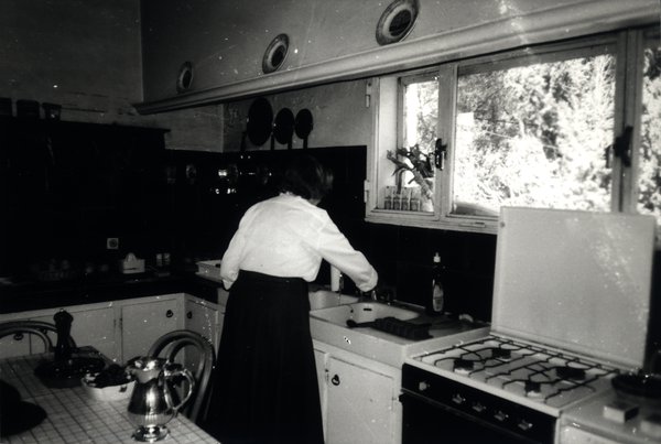 Femme de dos faisant la vaisselle dans une cuisine. Noir et blanc.ᴬᴵ