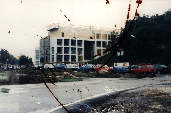 Bâtiment moderne en construction avec voitures garées sur le parking.ᴬᴵ