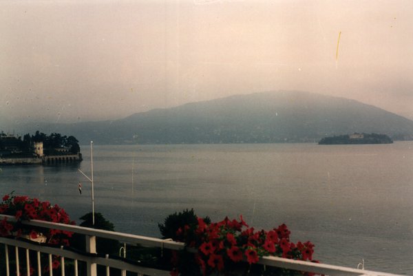 Vue sur un lac et ses collines depuis un balcon fleuri.ᴬᴵ