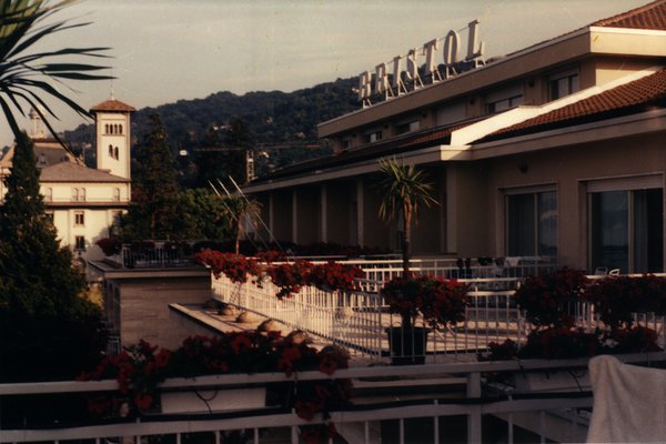 Terrasse de l'hôtel Bristol avec palmiers et fleurs rouges.ᴬᴵ