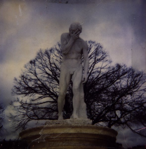 Statue d'un homme nu se couvrant le visage, devant un arbre dénudé.ᴬᴵ