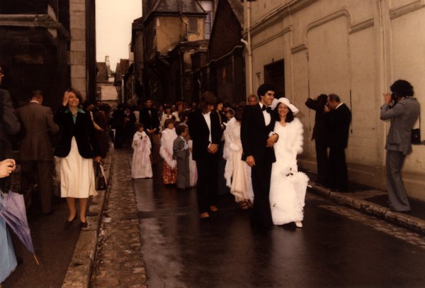 Cortège de mariage dans une rue pavée, invités en tenue de cérémonie.ᴬᴵ