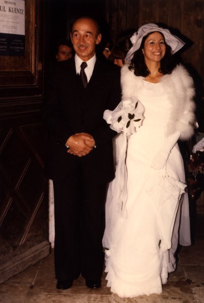 Mariée souriante au bras d'un homme âgé à l'entrée d'une église.ᴬᴵ