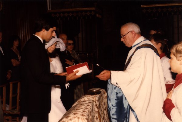 Prêtre en habits liturgiques remettant un livre aux mariés pendant la cérémonie.ᴬᴵ