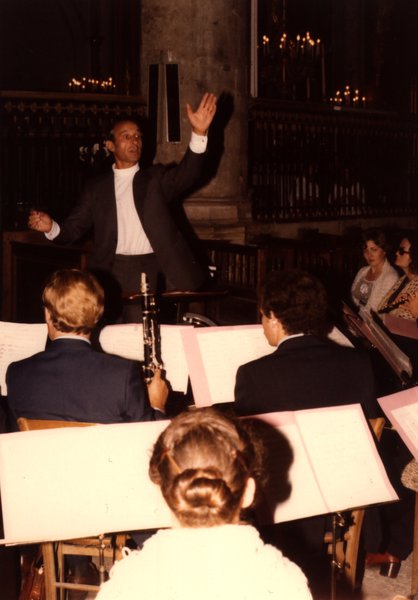 Chef d'orchestre bras levé dirigeant des musiciens dans une église, cierges en arrière-plan.ᴬᴵ