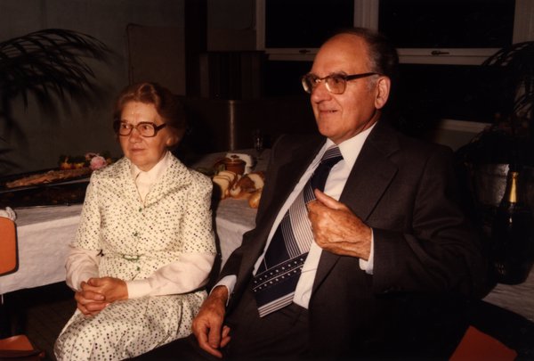 Couple âgé assis devant un buffet, femme en robe à pois.ᴬᴵ
