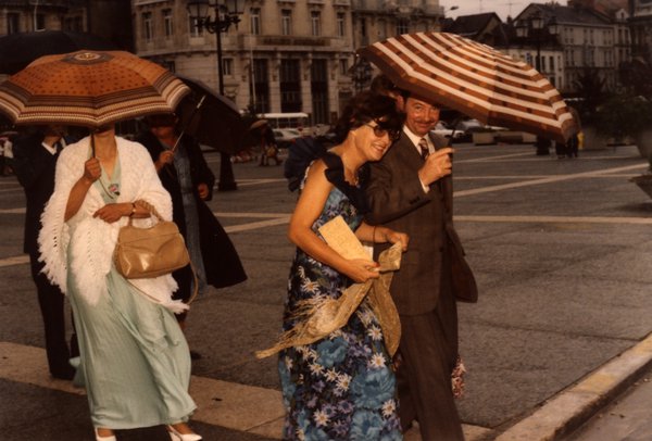 Invités de mariage avec parapluies sur une place, jour de pluie.ᴬᴵ