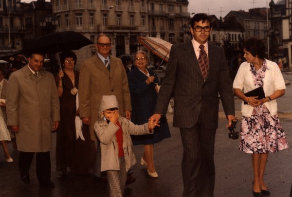 Groupe de mariage marchant sur une place sous la pluie, enfant tenu par la main.ᴬᴵ
