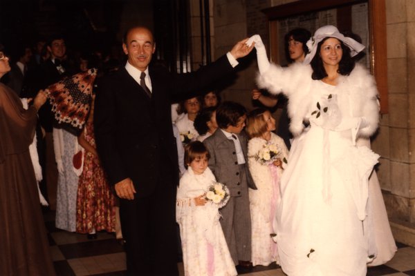 Mariée et homme en costume levant la main, entourés d'enfants avec bouquets.ᴬᴵ