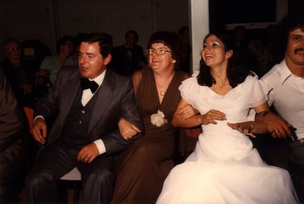 Groupe de convives riant, la mariée au premier plan, lors de la réception.ᴬᴵ