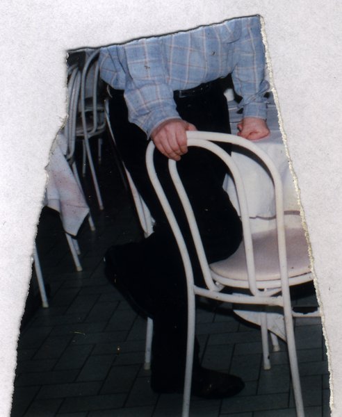 Homme assis sur une chaise en terrasse, vu de dos. Fragment déchiré.ᴬᴵ