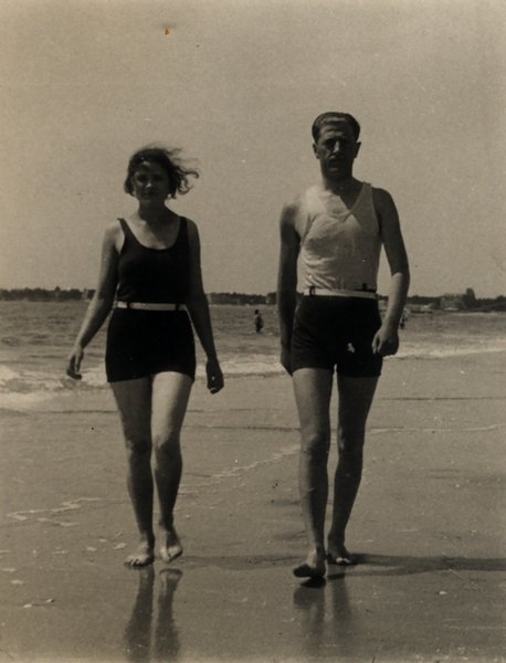 Homme et femme en maillot de bain ancien marchant pieds nus sur la plage. Noir et blanc.ᴬᴵ