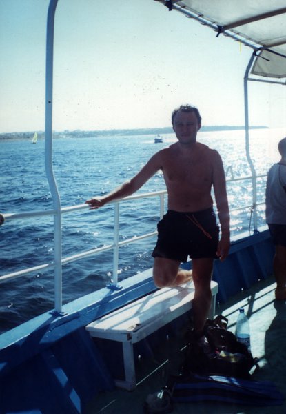 Homme torse nu sur un bateau, mer en arrière-plan.ᴬᴵ