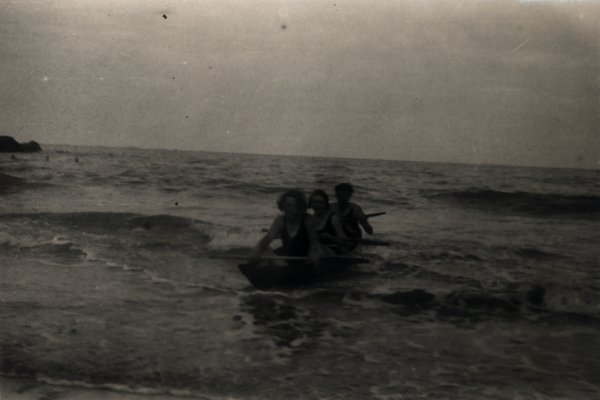 Trois personnes dans une barque près du rivage. Noir et blanc.ᴬᴵ