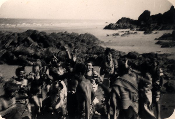 Groupe de personnes déguisées dansant parmi les rochers sur une plage, image floue. Noir et blanc.ᴬᴵ