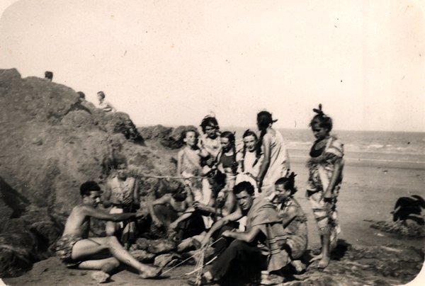 Groupe de personnes déguisées réunies sur une plage rocheuse. Noir et blanc.ᴬᴵ