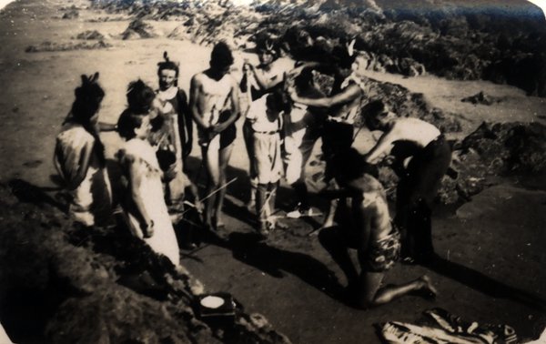 Groupe de personnes déguisées formant un cercle sur une plage. Noir et blanc.ᴬᴵ