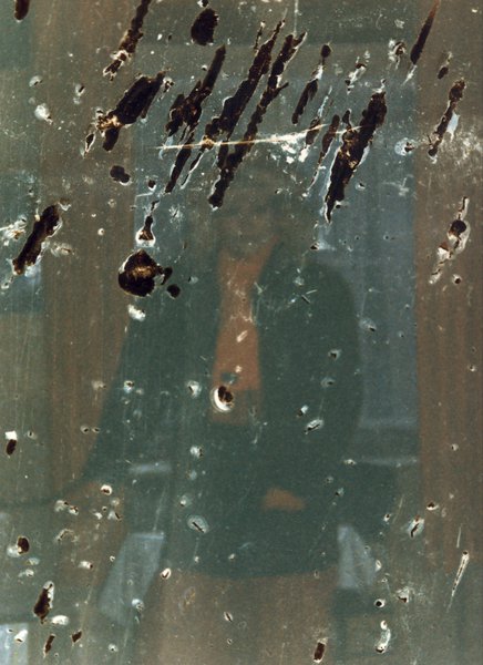 Femme blonde debout en blouson. Image abîmée.