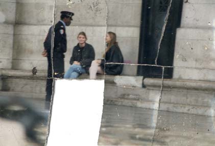 Deux adolescentes assisent sur un banc de pierre parlent à un policier. Image déchirée en partie reconstituée.