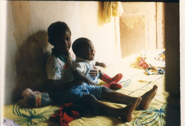 Petit garçon avec un enfant dans les bras assis sur un lit à parure jaune.