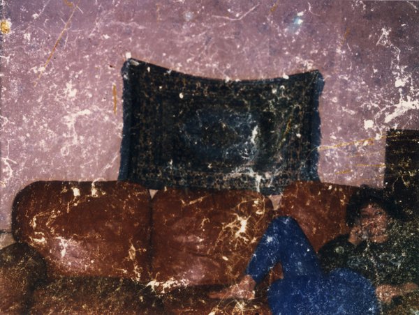 Femme brune allongée sur un canapé en cuir fauve, un téléphone à la main. Image abîmée.