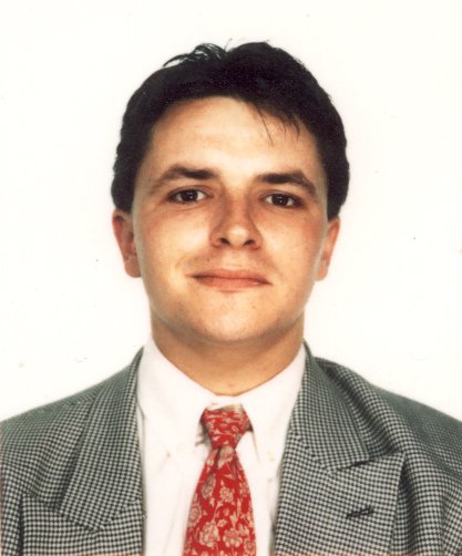 Visage d’homme brun souriant en costume et cravate rouge.