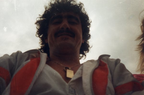 Homme Moustachu à cheveux bouclé en buste avec chaîne et pendentif autour du cou.