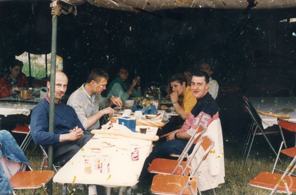 Hommes et femmes autour d’un repas sous une tente.