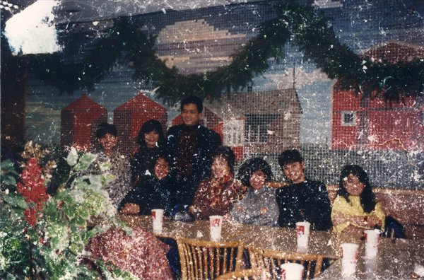Groupe d’hommes et de femmes posent autour d’une table. Image abîmée.