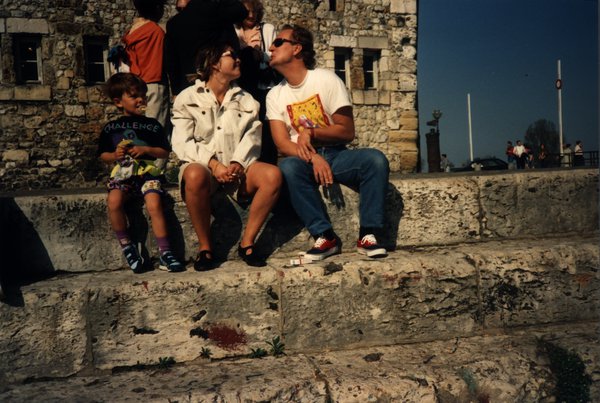 Couple s'embrassant assis sur un rempart, enfant à côté.ᴬᴵ