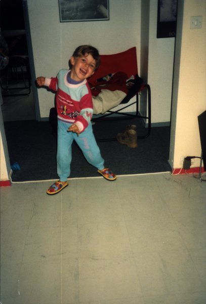 Enfant en pyjama souriant, bras écartés, dans un salon.ᴬᴵ