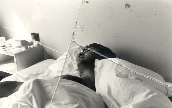 Homme brun couché dans un lit sous les draps. Noir et blanc. Image déchirée et reconstituée.