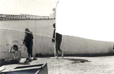 Trois individus en extérieur devant un mur. Noir et blanc. Image déchirée en partie reconstituée.
