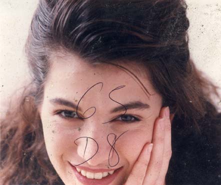 Visage de femme brune à cheveux longs souriante, une main sur la joue. Image avec inscription au bic bleu.