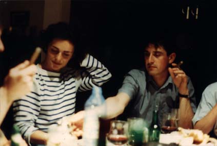 Hommes fumant un cigare et femme assise autour d’une table avec bouteilles et verres de vin.