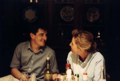 Homme brun et femme blonde assis côte à côte à une table où sont posés bouteilles.