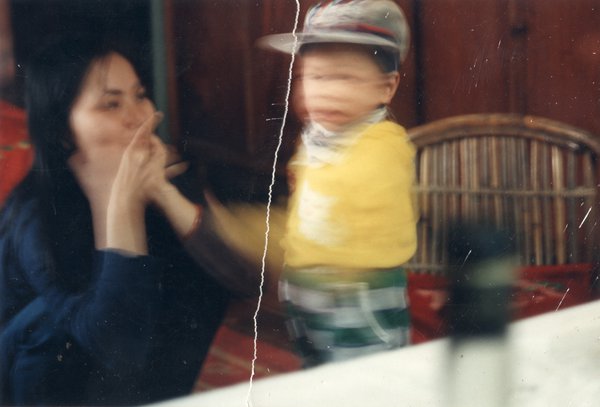 Femme et petit enfant avec un sweat jaune et une casquette. Image déchirée, reconstituée.