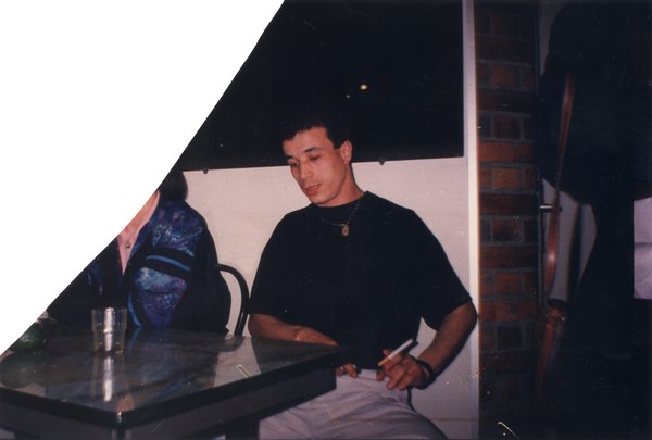 Homme assis avec une cigarette à une table de café. Image en partie déchirée.