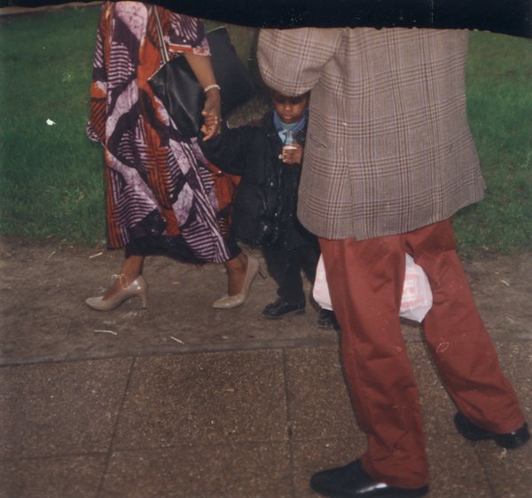 Jambes de femme en robe batik africaine avec un enfant, et jambes d’homme en costume.