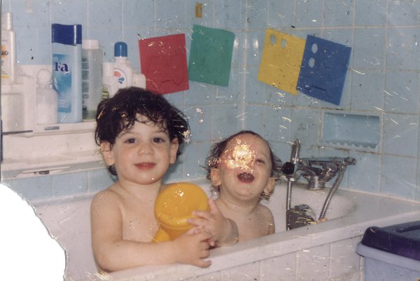 Deux enfants souriant nus dans une baignoire. Image déchirée.