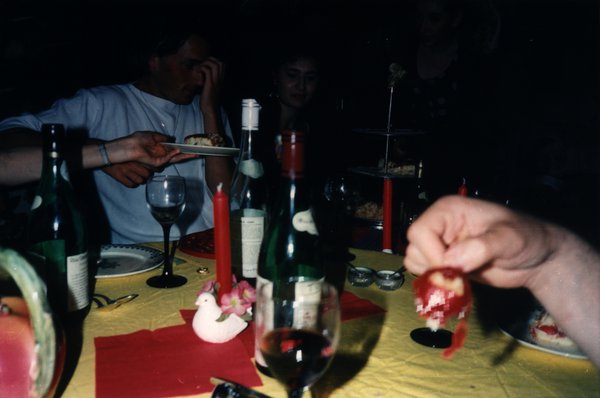 Main tenant un fruit au premier plan, dîner en arrière-plan avec bouteilles de vin.ᴬᴵ