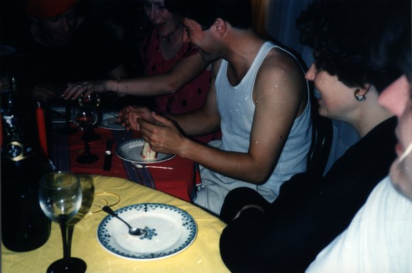 Homme mangeant un gâteau à une table de dîner, entouré de convives.ᴬᴵ