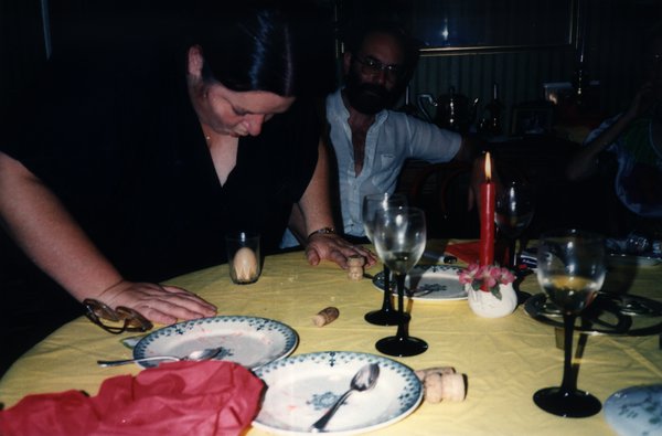 Femme et homme penchés au-dessus d'une table avec bouchons de liège et verres de vin.ᴬᴵ
