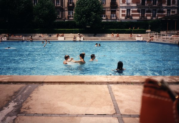 Piscine extérieure avec plusieurs baigneurs, immeubles en arrière-plan.ᴬᴵ