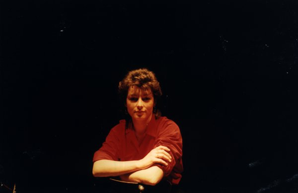 Portrait de femme en haut rouge, bras croisés, fond sombre.ᴬᴵ