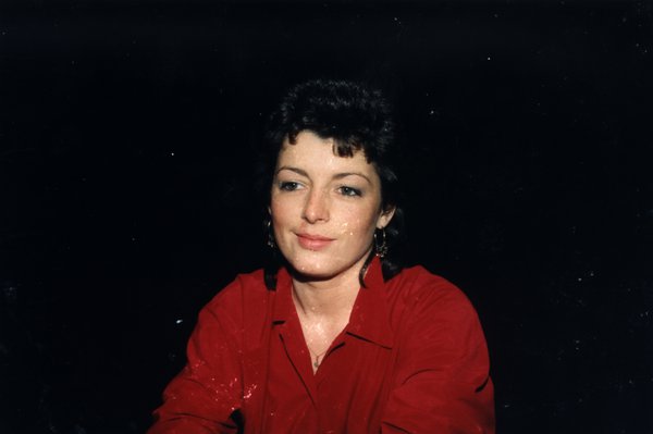 Portrait de femme en haut rouge souriant légèrement, fond sombre.ᴬᴵ