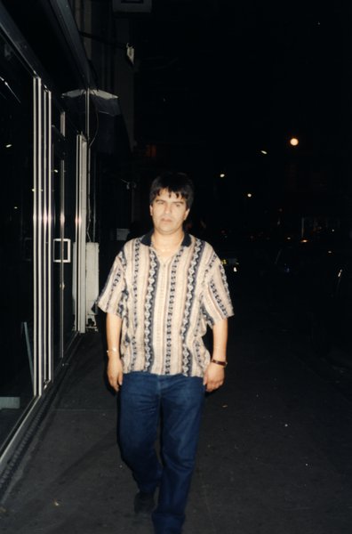 Homme marchant seul dans une rue de nuit devant des vitrines.ᴬᴵ